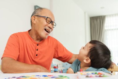 Asya 'nın son sınıf öğrencisi gözlüklü adam torunuyla ya da küçük oğluyla eğleniyor, paylaşılan aktivitelerle neşe ve bağlantı gösteriyor..