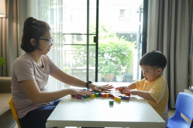 Asyalı anne ve küçük oğlu evlerinde renkli tahta bloklarla oynuyorlar, eğitici aktiviteler yapıyorlar, bağ kuruyorlar ve birlikte öğreniyorlar..