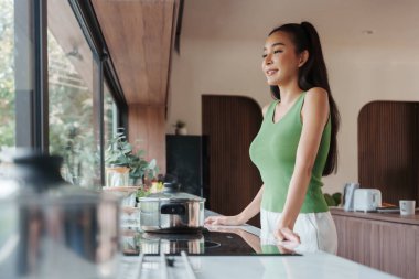 Yeşil kolsuz, rahat bir Asyalı kadın modern bir mutfakta yemek pişirmekten zevk alıyor.