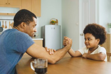 Siyah Afrikalı Amerikalı baba ve erkek bilek güreşi yapıyor. Sıradan bir ev hayatı. Aile bağı ve eğlenceli aktiviteler konsepti.