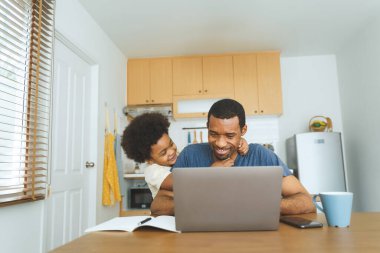 Siyah Afrikalı Amerikalı baba ve oğul, bilgisayar üzerinde çalışırken, aile bağlarını ve mutluluğu vurgulayarak mutfak masasında keyifli bir anı paylaşıyorlar..