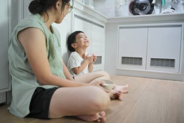 Asyalı bir kadın ve bir çocuk mutfakta yerde oturuyorlar..