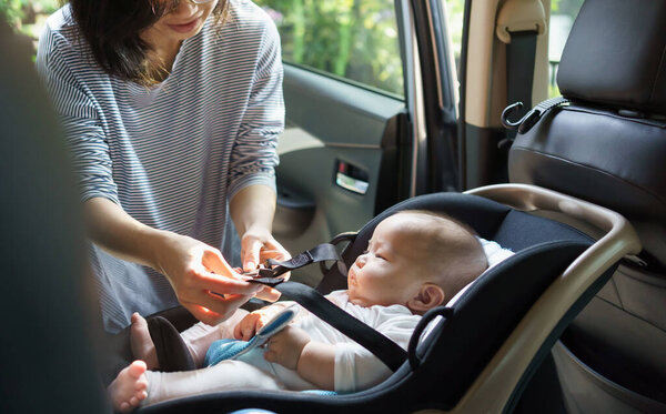 Азиатская мать закрепляет своего ребенка в автомобильном кресле на заднем сиденье автомобиля, обеспечивая безопасность.