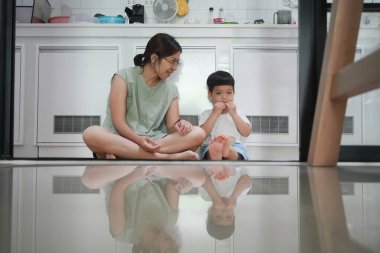 Asyalı bir anne ve bir çocuk mutfakta yerde oturmuş yemek yiyorlar..