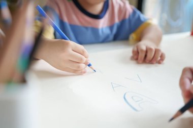 Yakın plan Asyalı çocuk, annesinin evinde renkli kalemle bir kağıt çiziyor..