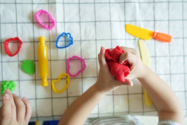 Üst düzey Asyalı çocuk oyun hamuru ve bıçakla oynuyor. Çocuk oyun hamurunu ellerinde tutuyor.