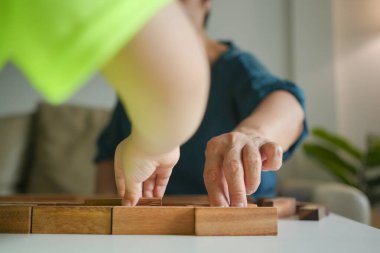 Bir çocuğun ve yaşlı bir kadının eli dikkatle masaya tahta bloklar yerleştiriyor..