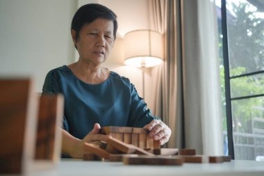 Asyalı yaşlı kadın, oturma odasındaki beyaz bir masaya tahta bloklar yerleştirirken konsantre oluyor..