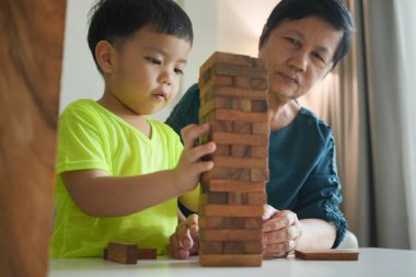 Yeşil tişörtlü Asyalı genç, yaşlı bir kadın ya da büyükanne tarafından nazikçe yönlendirilirken ahşap blokları dizmeye konsantre oluyor..