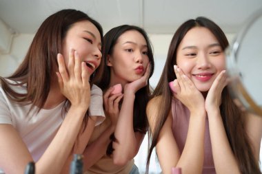 Cilt bakımından hoşlanan üç genç Asyalı kadın güzellik mikserleriyle makyaj yapıyorlar güzel kızlar aynanın karşısında gülümsüyor ve poz veriyorlar..