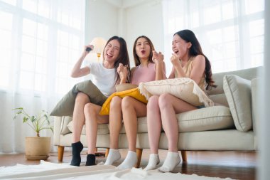 Arkadaşlık konsepti, üç Asyalı genç kadının oturma odasındaki kanepede tezahürat yapması ve kutlama yapması, genç kızların gülmesi ve gülümsemesi ve TV 'de birbirini eğlendiren heyecanlı bir olayı izlemesi..