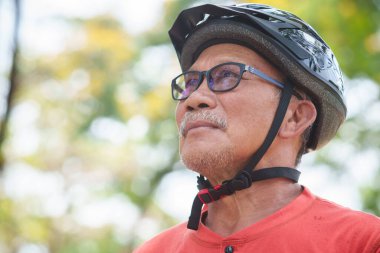 Gözlük ve koruyucu başlık takmış, turuncu gömlek giymiş, güneşli bir günün tadını çıkaran Asyalı kıdemli bisikletçi.