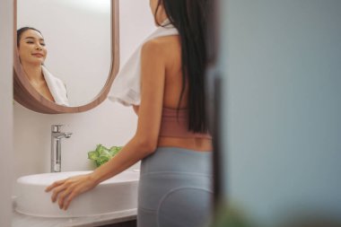 Spor kıyafetli Asyalı kadının portresi. Spor yaptıktan sonra havluyla banyo aynasının önünde.