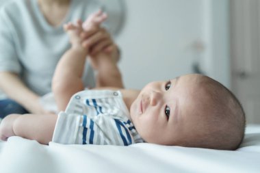 Asyalı anne bebek bezini bebek odasında bir yatakta değiştiriyor.