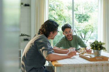 İki Asyalı adam bir masada oturmuş, akıllı bir telefonla sohbet ediyorlar. Mutfakta doğal ışık ve klasik dekorlarla dolu..