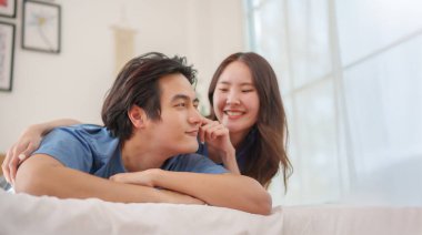 Genç Asyalı, oyuncu bir Çinli çift yatak odasında romantik bir anın tadını çıkarırken yatakta sıcak bir şekilde gülümsüyor..