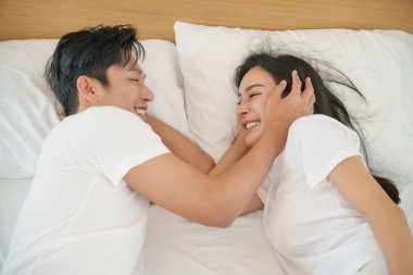 Oyuncu Asyalı çift yatakta samimi bir anı paylaşıyor, gülümsüyor ve sevgililer günü boyunca bir yatak odasında sevgi dolu bağlarının tadını çıkarıyorlar..