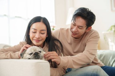 Asyalı çift rahat bir anın tadını çıkarıyor. Parlak oturma odasındaki rahat koltuklarında, mutluluk ve şefkat ifade ediyorlar.