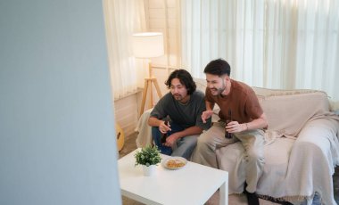 Oturma odasında bira içen iki Asyalı adam televizyonda odaklanmış ifadelerle futbol maçı izliyor. Futbol maçı olan iki arkadaş. Arkadaşlık kavramı