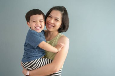 Asyalı anne ve çocuğun portresi gülüyor ve sarılıyor, neşeli ve sevgi dolu bir an yaratıyor.