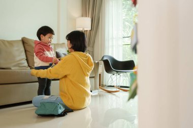 Asyalı küçük çocuk, annesiyle oturma odasında konuşurken gülümsüyor. Sabahları birlikte neşeli bir anın tadını çıkarıyor..