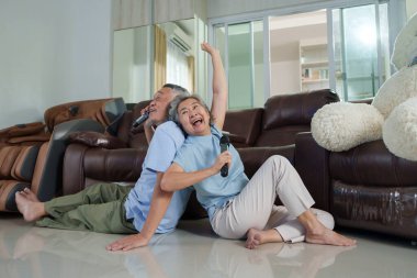 Asyalı son sınıf çifti evlerinde keyifle karaoke söylüyor, mikrofonlarıyla yerde oturuyor, rahat bir oturma odası dekoruyla çevrili. Mutluluğu ve birlikteliği ifade ederler.