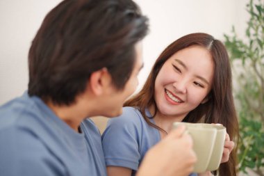 Gülümseyen Asyalı genç çift sıcak içeceklerin keyfini çıkarıyor, rahat ve neşeli bir atmosfer yaratıyor ve mutluluğu paylaşıyor.