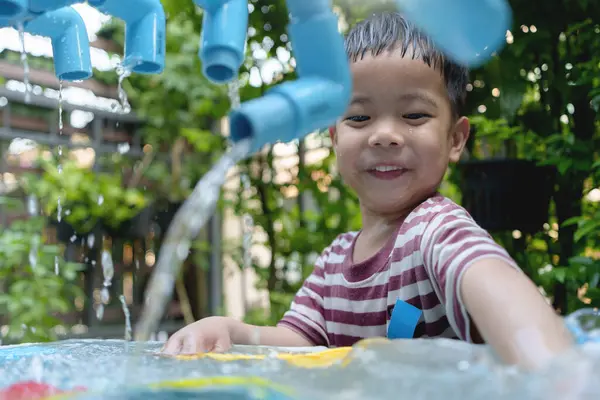 Çevresi yemyeşil yemyeşil, neşeli anlar yaratan, gülen yüzlü, su oyun alanında oynayan neşeli Asyalı çocuk..