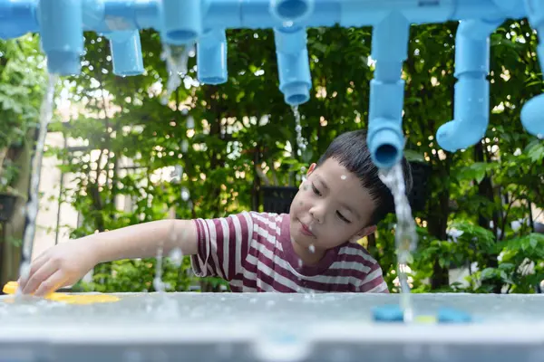 Çizgili tişörtlü genç Asyalı bir çocuk bir bahçe istasyonunda su oyunu oynuyor..