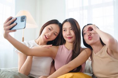 Üç Asyalı arkadaş akıllı telefonlarıyla selfie çekerken eğlenceli bir anın tadını çıkarıyorlar..