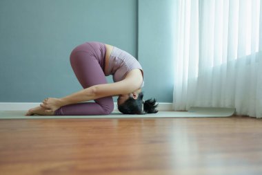 Asyalı kadın, yumuşak sabah ışığında sakin bir kapalı ortamda paspasın üzerinde zorlu bir yoga pozu veriyor..