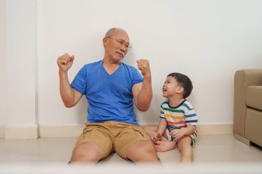 Asya 'nın son sınıf öğrencisiyle küçük bir çocuk, büyükbaba ve torunla birlikte neşe ve kahkaha dolu bir şekilde yerde eğleniyorlar..