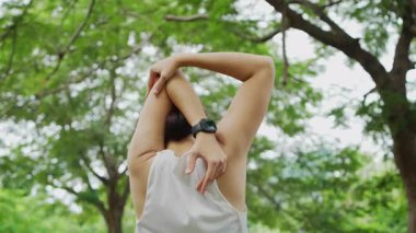 Yeşillik bir parkta egzersiz yapan Asyalı bir kadın. Fiziksel uygunluklarına ve sağlıklarına odaklanırken temiz hava ve güneş ışığının tadını çıkarıyorlar..