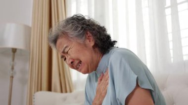 Yaşlı Asyalı kadın beyaz bir koltukta oturuyor, göğsü, acısı, endişesi, kalp krizi....