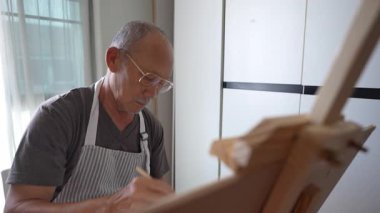 Asyalı son sınıf öğrencisi evde suluboya ile resim yapma becerisini geliştiriyor. Emeklilik yıllarında tutkusunu ve bağlılığını gösteriyor..