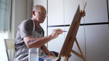 Asyalı son sınıf öğrencisi sanatına odaklanıyor. Evdeki suluboya boyayla kağıda dikkatlice boya sürüyor..