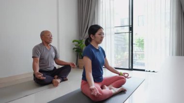 Asyalı üst düzey erkek ve kadın evlerinde yoga yapıyorlar, günlük emeklilik rutinlerinde rahatlama, farkındalık ve sağlığa odaklanıyorlar..