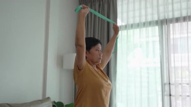 Üst düzey bir Asyalı kadın evde televizyondaki bir çevrimiçi dersi takip ederken direniş grubuyla egzersiz yapıyor..