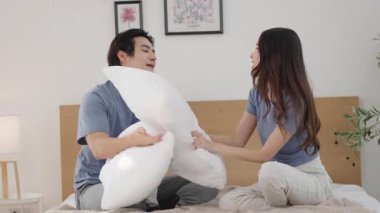 Asyalı çift, sabahları yataklarını yatak odalarında toplarken yastık savaşı yapmaktan zevk alıyor..