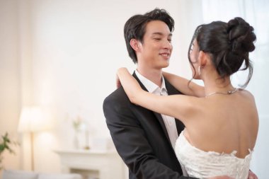 Asyalı gelin ve damat birbirlerini incelerken gülümseyerek nazik bir anı paylaşırlar. Aşk ve bağlarla dolu romantik bir an. Çiftler güzel bir evlilik yıldönümünü paylaşıyor..