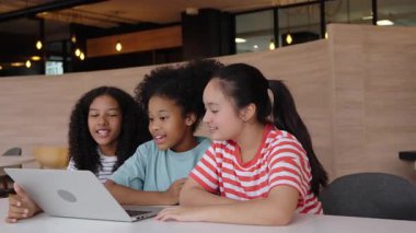 Sınıfta dizüstü bilgisayarla çalışırken başarıyı kutlayan üç neşeli kız çoklu etnik çocuklar dijital teknolojiyle öğrenme sevincini ve heyecanını gösteriyorlar.