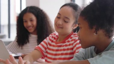 Gülümseyen üç farklı küçük kız bir sınıfta dizüstü bilgisayarda birlikte öğreniyorlar, eğleniyorlar, E-öğrenim ve online eğitim sınıfında çoklu etnik çocuklar gösteriyorlar..