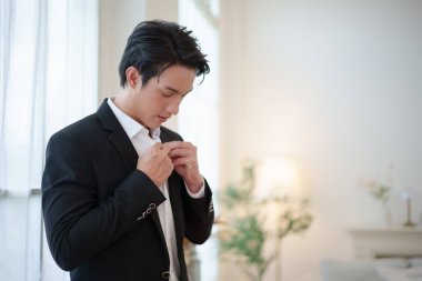 Asyalı damat şık bir takım elbise ayarlar ve aşağı bakar. Düğün törenine özgüvenle hazırlanırken..