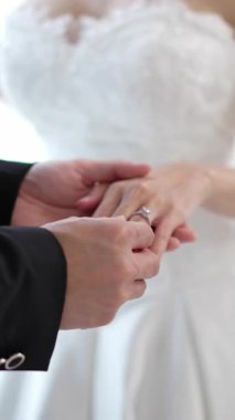 Romantik damadın gelin parmağına yüzük taktığı, zarif Asyalı çiftin özel tören gününde aşkı paylaştığı yakın plan.