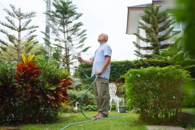 Mutlu Asyalı son sınıf öğrencisi erkek bahçesinde bitkileri suluyor. Yaşlı adam bahçeyle uğraşmayı sever..