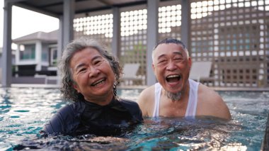 Yüzme havuzunda gülümseyen mutlu Asyalı son sınıf çifti. Yaşlı adam ve kadın neşe içinde birlikte eğleniyor ve gülüyorlar..