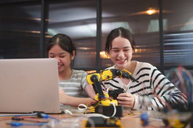 Gülümseyen öğrenciler STEM öğreniminde takım çalışması ve eğlence gösteren bir robot kolu yapıp programlıyorlar..