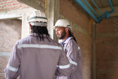 Afrikalı mühendisler inşaat alanında bir arada duruyorlar, takım çalışması ve kendine güvenen tavırlarla iş ilerlemelerini konuşuyorlar ve kontrol ediyorlar..
