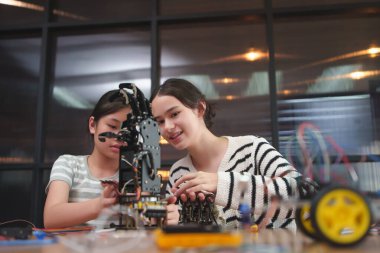 Çeşitli kızlar bir STEM projesi için robotik bir kol yapıyor, sınıfta takım çalışması, teknoloji ve mühendisliği birlikte öğrenip eğleniyorlar..