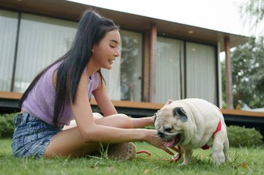 Asyalı bir kadın çimenlerin üzerinde köpeğiyle oynuyor, dışarıda mutlu ve enerjik bir anın tadını çıkarıyor..